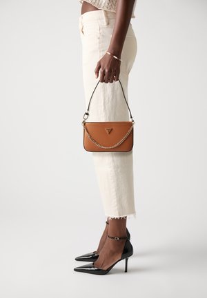 Brown leather handbag with a chain strap, featuring a triangular logo. Worn with light-colored cropped pants and black pointed-toe heels.