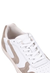 Weißer Sneaker mit Veloursleder-Akzenten in Hellbeige, perforierter Zehenkappe und flachen Schnürsenkeln. Weiches Innenfutter und geschwungenes Design.