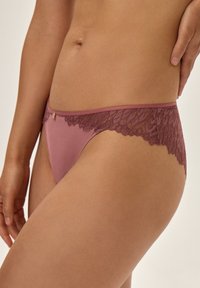 Majtkę w kolorze mauve z koronką i satyną, z kwiecistym koronkowym wykończeniem w pasie oraz subtelnym złotym akcentem. Gładka tekstura, dopasowany krój.