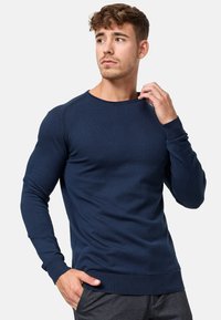 Pull en maille bleu marine à manches longues, col ras du cou, fabriqué dans un tissu doux, avec des poignets et un ourlet côtelés, une silhouette ajustée et des détails de coutures minimaux.