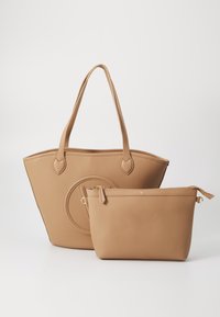 Καφέ δερμάτινη τσάντα tote με υφή, στρογγυλό σχήμα, δύο λαβές και ένα αντίστοιχο τσαντάκι με φερμουάρ. Εντυπωσιακό κυκλικό διακοσμητικό στοιχείο στο μπροστά μέρος.