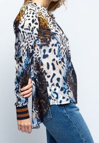 Camisa de estampado de leopardo en tonos multicolores de beige, marrón y azul, con mangas largas y un dobladillo curvado con puños a rayas.
