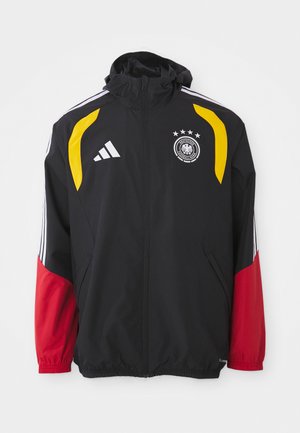 Melnā sportiskā jaka ar rāvējslēdzēju, dzelteniem akcentiem, sarkaniem piedurknēm, baltām svītrām, Adidas logotipu un Vācijas futbola asociācijas emblemu ar četriem zvaigznēm.