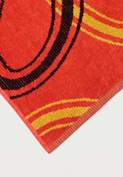 Φωτεινό κόκκινο ύφασμα με μαύρες και κίτρινες συγκεντρικές καμπυλωτές γραμμές και υφασμένο υλικό με υφή, εμφανιζόμενο σε γωνία.