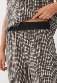 Zwart-wit gemêleerde top met een losse pasvorm en geribbelde zwarte tailleband, gecombineerd met bijpassende wijde broek die hetzelfde patroon heeft.