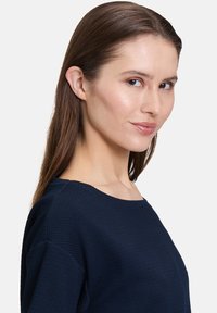 Navy blue wzorzysty top z szerokim dekoltem, z długimi rękawami i luźnym krojem, zaprezentowany na modelce z boku.