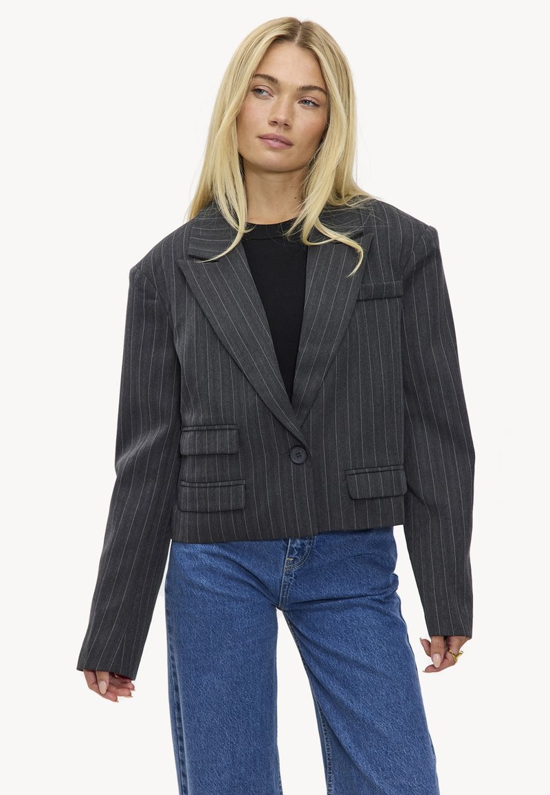 Blazer noir coupé avec un motif à fines rayures, à larges revers, fermeture à un bouton et deux poches avant. Associé à un jean taille haute bleu clair.