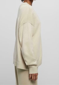 Ljust beige tröja med lös passform, ribbade ärmslut och nederkant, texturerad stickad tyg, och en subtil, oversized design.