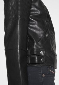 Schwarze Leder-Motorradjacke mit gesteppten Schulterakzenten, silberner Hardware und verstellbaren seitlichen Riemen für eine optimale Passform.