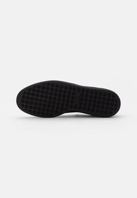 Suela de zapato de goma negra con una superficie texturizada que presenta patrones triangulares repetidos para tracción y durabilidad.