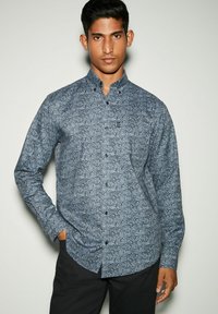 Camisetta a maniche lunghe di colore blu navy con un motivo paisley, dotata di colletto a camicia e bottoni neri. Il tessuto appare liscio e leggero.