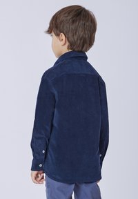 Camicia in velluto a coste blu navy con colletto, maniche lunghe e polsini con bottoni. Tessuto liscio e dettaglio dell'orlo arrotondato sul retro.