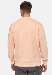 Lyserød sweatshirt med rund hals og lange ærmer, prydet med et enkelt design samt ribbestrikket kant og manchetter, lavet af blødt stof.