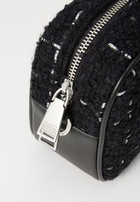 Μαύρη τσάντα από ύφασμα με υφή, με ασημένιο φερμουάρ και μεταλλικό κούμπωμα. Διαθέτει λεπτομέρειες λογότυπου σε λευκό χρώμα στο ύφασμα.