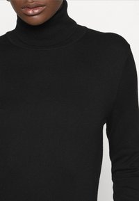 Svart turtleneck-tröja i mjukt stickat material, med långa ärmar och ribbad halsringning. Närbild som framhäver textur och passform.