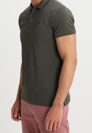 Polo vert foncé à manches courtes, avec un col roulé et un petit logo sur la poitrine. Confectionné en mélange de coton texturé.