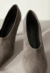 Chaussures à talons hauts en daim gris avec un design à bout pointu, présentant une texture lisse et des semelles intérieures noires.