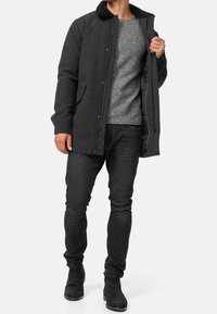 Grå frakke med sort krave, lynlåslukning, sidelommer; båret over en lysegrå sweater og sorte jeans; sorte støvler fuldender looket.