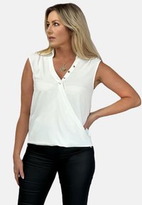 Biała bezrękawnikowa bluzka o fasonie kopertowym, z zapięciem na guziki, gładką teksturą, zestawiona z czarnymi dopasowanymi spodniami.