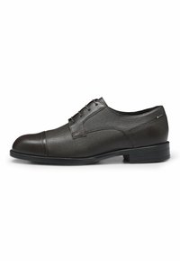 Scarpa elegante in pelle marrone con finitura texture, punta rotonda, design con lacci e suola nera a contrasto. Leggero accento del marchio visibile.