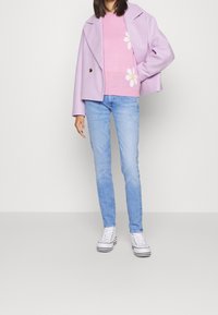 Lila ullblandad kappa, rosa stickad tröja med vita blommönster, ljusblå denimjeans och vita sneakers med svarta ränder.