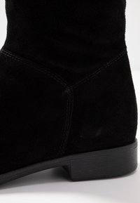 Czarne zamszowe botki sięgające kostki z niskim obcasem, gładką fakturą i przeszyciem, o zaokrąglonym kształcie w okolicy kostki.
