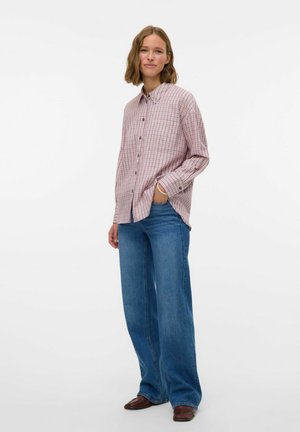 Ruitjesoverhemd in rood en wit met knoopsluiting, lange mouwen en een relaxte fit, gedragen met wijde blauwe jeans en bruine schoenen.