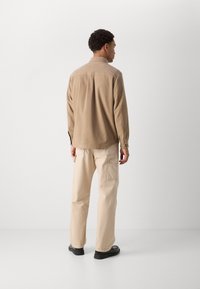 Chemise beige à manches longues avec un col, texture de tissu et poignets boutonnés ; associée à un pantalon cargo de couleur claire avec des poches latérales.
