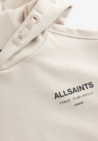 Felpa con cappuccio beige in tessuto morbido, con collo regolabile a coulisse, logo stampato "ALLSAINTS" e elementi di design minimalisti.