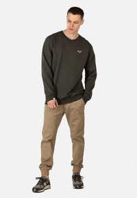Donkergroen katoenen sweatshirt met ronde hals, ribgebreide boorden en zoom, gedragen met beige taps toelopende broek en grijze schoenen met zwarte accenten.