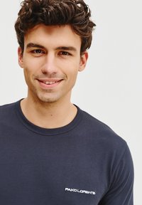 Granatowa koszulka z miękkiej bawełny, z okrągłym dekoltem i małym białym haftowanym logo po lewej stronie.