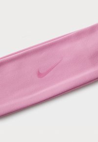 Un bandeau rose Nike en tissu doux et lisse présente un logo subtil en relief. Le design est étroit et allongé, parfait pour maintenir les cheveux en place.