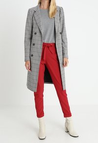 Lang, dobbeltradet frakke i sort og hvid houndstooth, parret med røde, højtaljede tapered bukser og beige ankelstøvler.