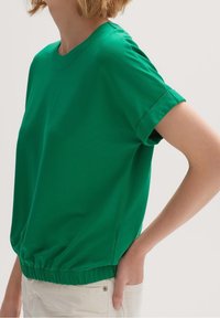 Grøn kortærmet top med rund halsudskæring og elastisk kant. Lavet af blødt stof med en afslappet pasform og med opsmøgede ærmer.