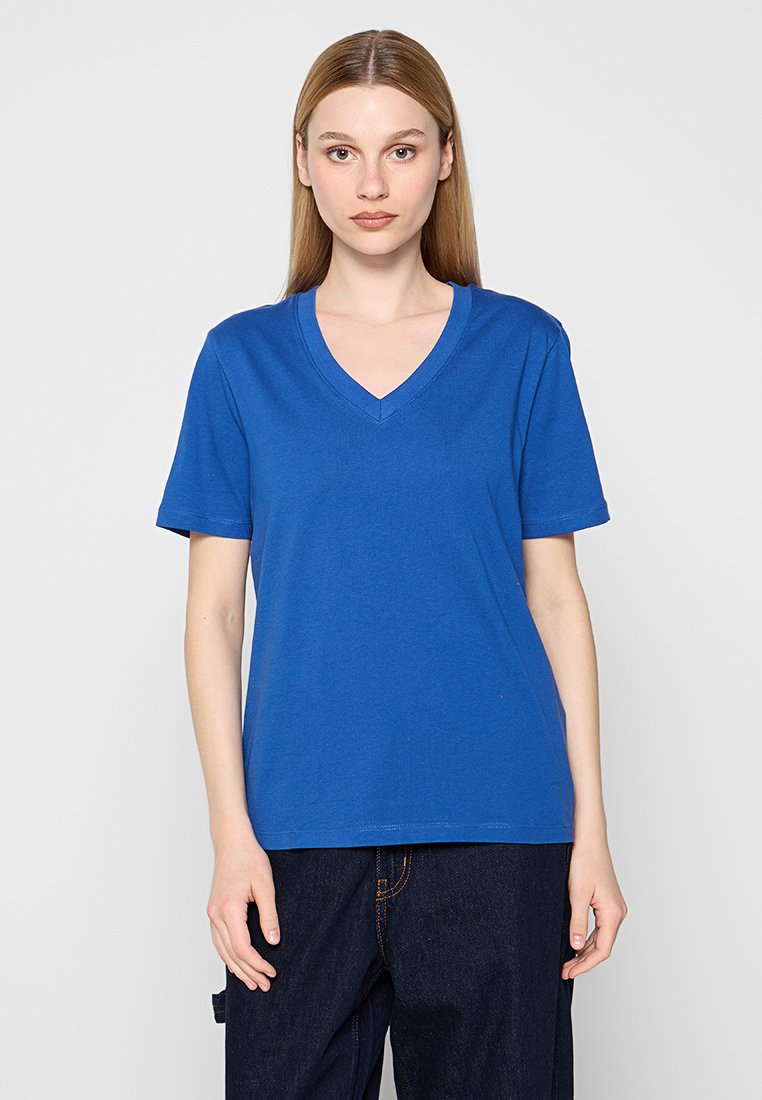T-shirt z dekoltem w serek, krótki rękaw, w jasnoniebieskim kolorze z bawełny, charakteryzujący się luźnym krojem i gładką teksturą, zestawiony z ciemnoniebieskimi dżinsami.