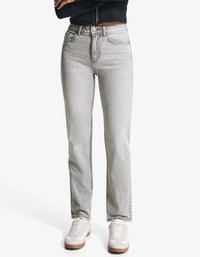 Sive visoke traperice ravnog kroja, s pet džepova i laganim oštećenjima, u kombinaciji s bijelim tenisicama.