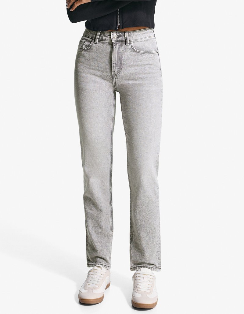 Sive visoke traperice ravnog kroja, s pet džepova i laganim oštećenjima, u kombinaciji s bijelim tenisicama.