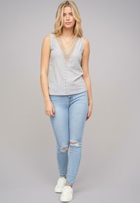 Top fără mâneci de culoare gri deschis, cu decolteu în V, având detalii cu găuri decorative. Asortat cu blugi skinny rupti de culoare albastră deschisă și adidași albi.