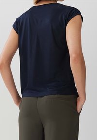 Námořnická modrá tričko s krátkým rukávem a kulatým výstřihem, vyrobené z hladkého materiálu, v kombinaci se olivově zelenými kalhotami. Jednoduchý a klasický design.