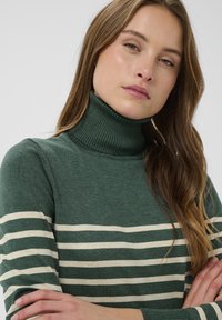 Zeleni pulover s turtleneck iz mehkega pletenega materiala, okrašen s kremnimi vodoravnimi črtami; ima prilegajočo zasnovo in rebrast ovratnik.