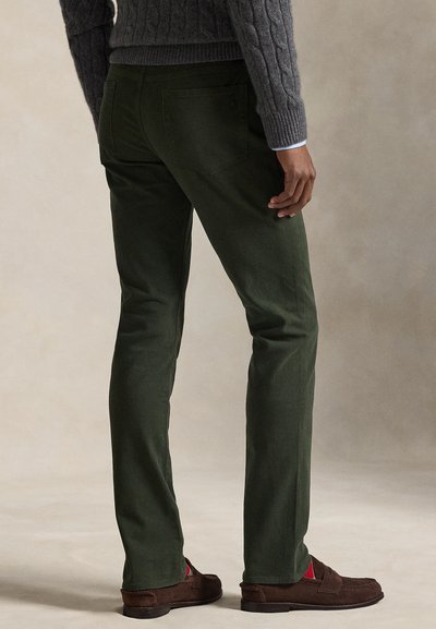 Σκούρο πράσινο παντελόνι από κορντόρι με στενή γραμμή, που έχει δύο τσέπες στην πλάτη, σε συνδυασμό με καφέ μοκασίνια και πλεκτό γκρι πουλόβερ με υφή.