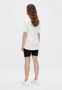 Haut blanc à manches courtes avec un ourlet arrondi, associé à un short de vélo noir et des baskets blanches. Cheveux longs et ondulés coiffés lâchés.