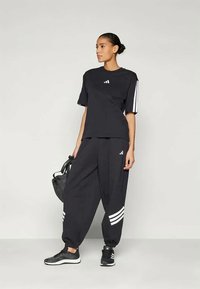 Mustlane sportlik komplekt, mis koosneb T-särgist ja lõtvatest pükstest, millel on valged triibud, valmistatud siledast kangast, ning sobitatud mustade sneakerite ja kotiga.