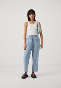 Light blue tapered pants with an elastic waistband, paired with a white ribbed tank top and black strappy sandals. A small blue shoulder bag completes the look.