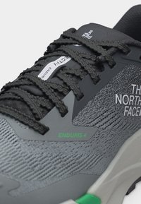 Γκρι και μαύρο αθλητικό παπούτσι North Face Enduris 4 με υφή υφάσματος, μαύρα κορδόνια και πράσινη λεπτομέρεια στη σόλα.