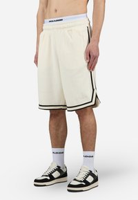 Kremfargede shorts med et teksturert mønster, svarte sidelister og svart kant. Kombinert med svarte og hvite sneakers og hvite sokker.