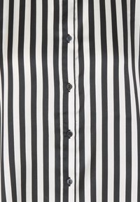 Svart och vit vertikalt randig tyg med en mittstående rad av fem svarta knappar knäppta, som visar lätta tygveck.