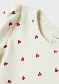 Chemise blanche à manches courtes avec un col rond, ornée de motifs de cœurs en paillettes rouges éparpillés et de légères manches bouffantes.