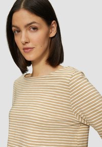 Gestreiftes Top in Beige und Weiß mit rundem Ausschnitt und drei Viertelärmeln, hergestellt aus einem weichen Baumwollstoff mit glatter Textur.
