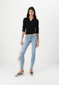 Black ribbed long-sleeve top paired with light blue skinny jeans and silver pointed shoes. Model holds a metallic handbag.